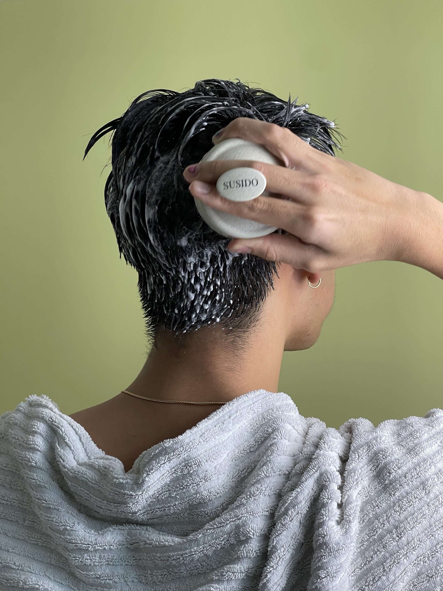 Person mit nassen Haaren, die eine plastikfreie Kopfhautbürste 🧖‍♂️ verwendet, um die Kopfhaut zu massieren und zu pflegen.